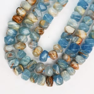 May include: A strand of tumbled, irregular-shaped beads in shades of translucent blue, white, and brown. The beads are strung on a thin blue thread, showcasing a smooth, polished surface with natural color variations and organic, rounded edges.