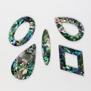 Könnte beinhalten: Fünf schillernde Abalone-Muschel-Anhänger in verschiedenen Formen: ein Oval, ein Tropfen, ein langes Oval, ein Tropfen und eine Raute. Die Anhänger haben eine Mischung aus grünen, blauen und violetten Farben.