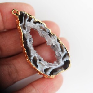 May include: A gold-rimmed agate pendant with a large, open center. The agate is white and gray with black banding.