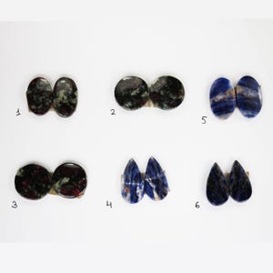Peut inclure: Six paires de cabochons de pierres précieuses, deux de chaque couleur verte et noire, bleue et blanche, et bleue. Les cabochons sont disposés en rangées de deux, avec les numéros 1 à 6 sous chaque paire.
