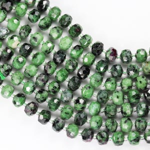 May include: A strand of green, faceted, gemstone beads with black and red inclusions. The beads are approximately 6mm in size and have a polished finish.