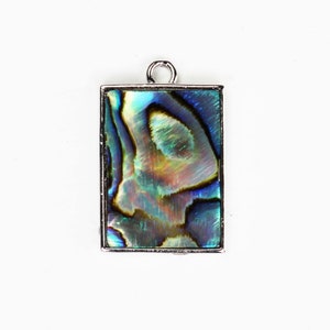 May include: A silver pendant with a rectangular abalone shell inlay. The shell has iridescent blue, green, and gold colors.