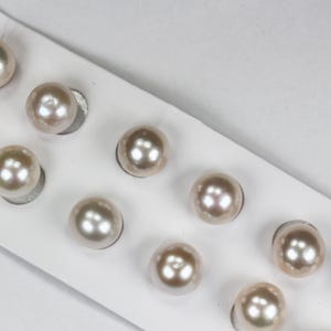May include: Close-up of several lustrous, round pearls. The pearls are a soft, creamy color with subtle iridescence. They are set on a white surface, suggesting a jewelry display or presentation.