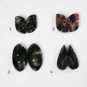 May include: Four pairs of cabochon gemstone earrings. The first pair is black and white with a speckled pattern. The second pair is pink and black with a speckled pattern. The third pair is green and black with a speckled pattern. The fourth pair is black with a speckled pattern.