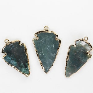 May include: Three gemstone arrowhead pendants with gold-coloured edging. The pendants have a dark green and white mottled appearance. Each pendant has a small loop at the top for hanging.
