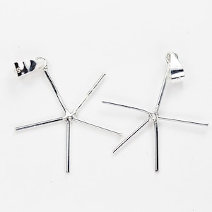 May include: Two silver-coloured metal pendant settings, each featuring a five-prong star-shaped basket design with a triangular bail at the top. The prongs are thin, straight, and extend outward from a central point to hold a gemstone.