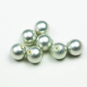 May include: A group of eight light green pearl beads with a hole in the centre of each bead.