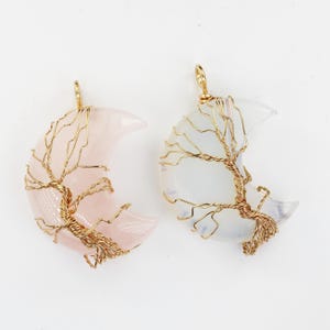 May include: Two crescent moon shaped pendants with gold wire tree of life designs. One pendant is made of rose quartz and the other is made of white opal.