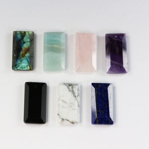 May include: Seven rectangular gemstone pendants in various colours, including black, white, green, blue, pink, and purple. The pendants are all approximately 5 cm long and have a hole at the top for hanging.
