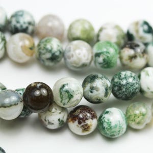 May include: A strand of round, green, white and brown moss agate beads. The beads are approximately 8mm in diameter.