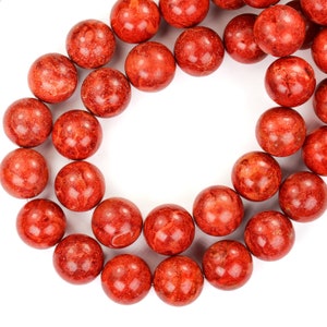 Peut inclure: Un collier de perles de corail rouge, chaque perle est ronde et a une surface texturée.