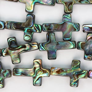 May include: A collection of cross-shaped beads crafted from iridescent abalone shell. Each bead displays a unique, swirling pattern of deep greens, blues, purples, and metallic gold tones, reflecting light with a polished, pearlescent finish.