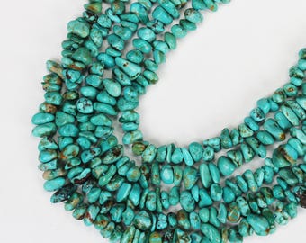 Può includere: Primo piano di una collana turchese. La collana è composta da piccole perle di turchese di forma irregolare. Le perle sono di un vibrante colore turchese con alcune inclusioni marroni e nere. La collana è esposta su uno sfondo bianco.