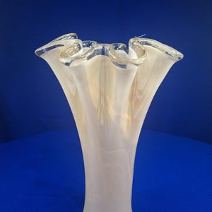 May include: A tall glass vase with a flared, ruffled rim. The vase features a translucent, creamy off-white color with subtle, swirling beige and tan internal patterns that create a soft, layered effect throughout the smooth, curved body.