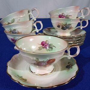 May include: Set of six vintage teacups and saucers with a floral design featuring fruit and berries. The cups and saucers are white with a light green and pink glaze. The floral design is in shades of pink, red, and purple.