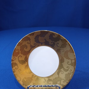 May include: A gold saucer with a white center and a swirling cloud pattern. The saucer is on a blue surface.
