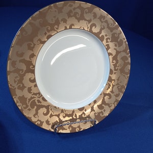 May include: A white ceramic dinner plate with a gold rim and a swirling cloud pattern.