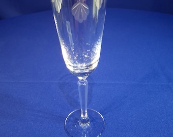 May include: A clear glass champagne flute with a gold rim and etched floral design. The flute is on a blue background.