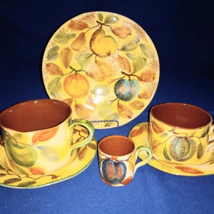 May include: A set of four yellow ceramic teacups and saucers with a fruit design. The cups and saucers feature a yellow background with green leaves, red berries, and yellow and blue fruit. The set includes a small teacup and saucer.