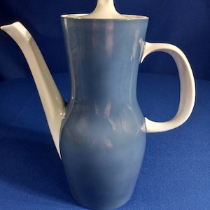 May include: A ceramic coffee pot with a blue body and white accents. The pot features a curved spout, a handle, and a lid with a knob. The design is sleek and modern, suitable for serving coffee or tea.
