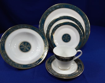 May include: A set of five white porcelain plates with a green and gold floral design. The plates are arranged in a pyramid shape, with the largest plate at the bottom and the smallest plate at the top. A white porcelain teacup and saucer with a matching design are in front of the plates.