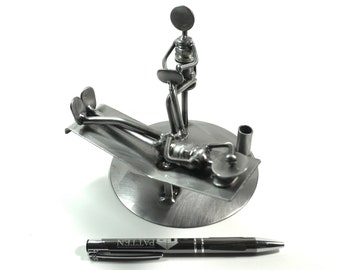 May include: A metal sculpture of a doctor examining a patient on a table. The sculpture is made of nuts, bolts, and other metal pieces. The doctor is standing and the patient is lying down. The sculpture is on a round base.