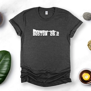 May include: A dark gray t-shirt with a white graphic of the Boston skyline and the text "BOSTON 26.2".