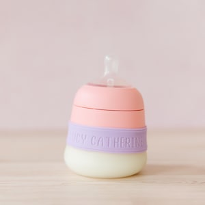 Puede incluir: Un biberón rosa y morado con una tetina transparente y una banda morada que dice "Lucy Catherine".