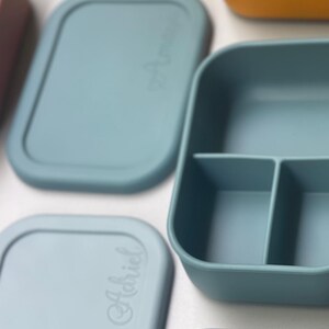 May include: A set of four blue silicone food containers with lids. The containers have different compartments and are labeled with the word "Habiciel".