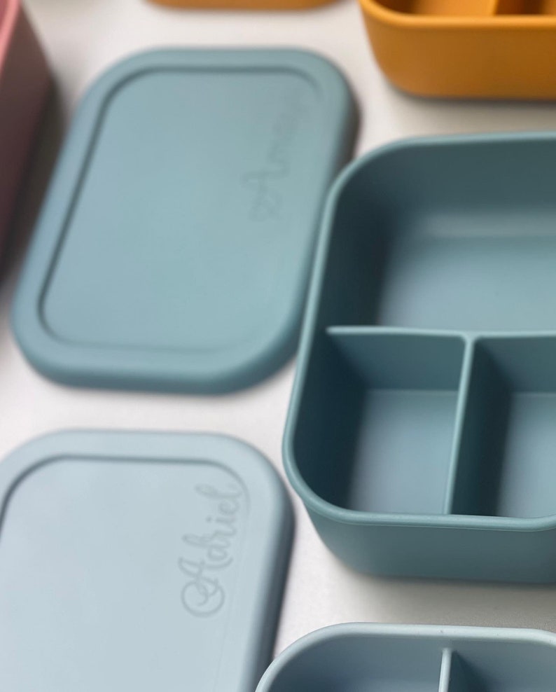 May include: A set of four blue silicone food containers with lids. The containers have different compartments and are labeled with the word "Habiciel".