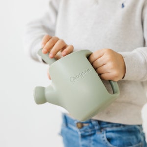 Puede incluir: Una regadera de plástico verde claro con asa y boquilla. La regadera tiene el nombre "Grayson" grabado en el lateral.