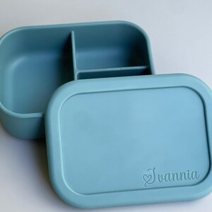 May include: A light blue silicone lunch box with three compartments and a lid. The lid has the name "Ivanni" engraved on it.