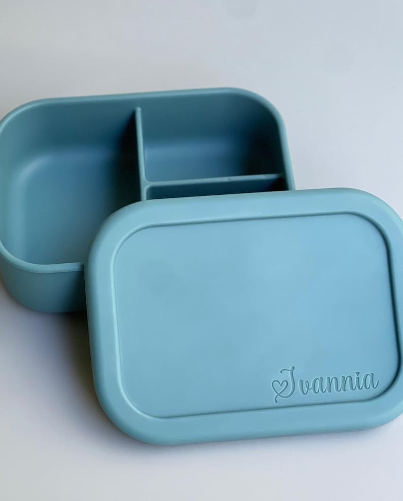 May include: A light blue silicone lunch box with three compartments and a lid. The lid has the name "Ivanni" engraved on it.