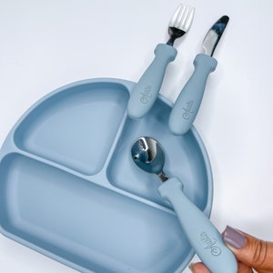 May include: A blue silicone divided plate with a fork, knife, and spoon. The utensils have blue handles with the word "Austin" printed on them.