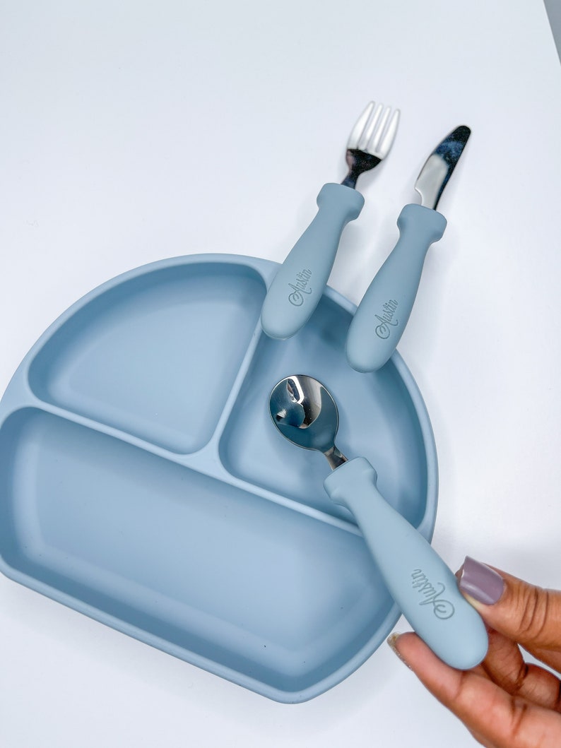 May include: A blue silicone divided plate with a fork, knife, and spoon. The utensils have blue handles with the word "Austin" printed on them.