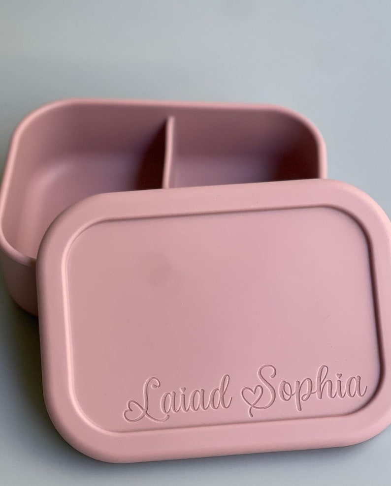 May include: A pink silicone lunch box with a divided interior and a lid that has the name "Laiad Sophia" engraved on it.