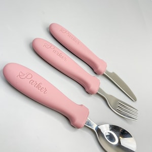 May include: A set of three pink baby utensils with a heart and the name "Parker" engraved on the handles. The set includes a spoon, fork, and knife.