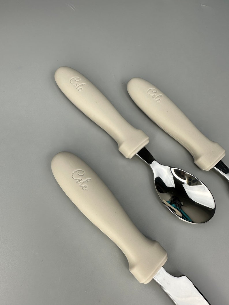 May include: Three white handled utensils with the word "Cole" embossed on the handles. The utensils are a spoon, a knife, and a fork.