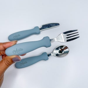 May include: A set of three blue baby utensils with the name "Austin" engraved on the handles. The set includes a fork, knife, and spoon.