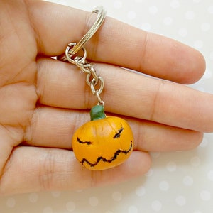 May include: A small orange pumpkin with a black jack-o'-lantern face is attached to a silver key chain.