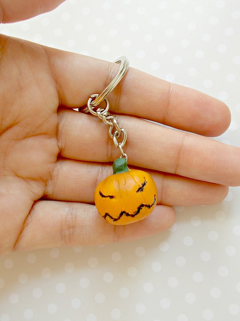 May include: A small orange pumpkin with a black jack-o'-lantern face is attached to a silver key chain.