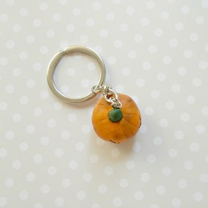 May include: A small orange pumpkin keychain with a green stem and a silver key ring.