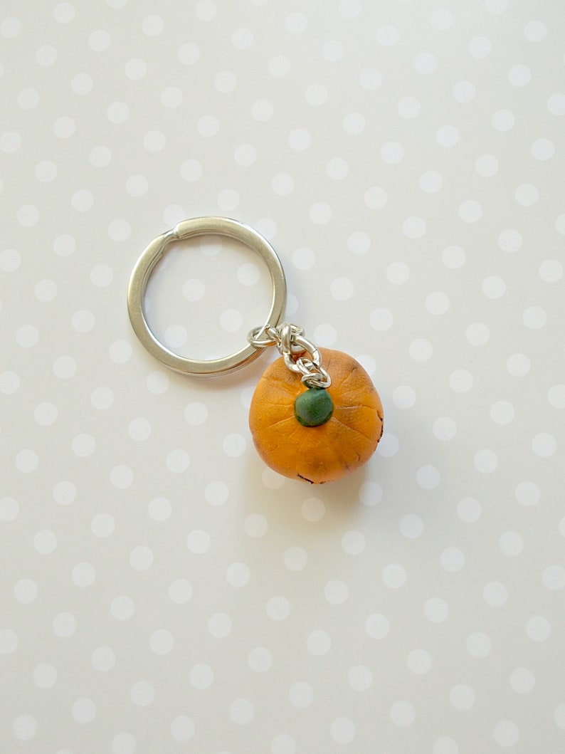 May include: A small orange pumpkin keychain with a green stem and a silver key ring.
