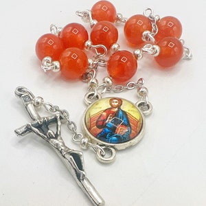 Könnte beinhalten: Eine silberne Rosenkranz mit orangefarbenen Perlen und einem silbernen Kruzifix. Das Mittelstück zeigt ein rundes Bild von Jesus.