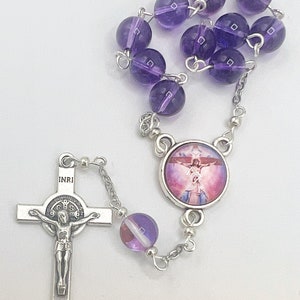 May include: A purple amethyst rosary with a silver crucifix and a round silver pendant featuring a depiction of Jesus Christ. The pendant has a pink and white background.