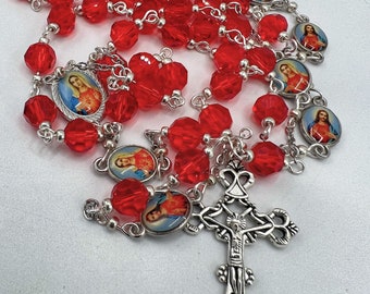 May include: Red crystal rosary beads with silver accents and a silver crucifix. The beads feature small images of Jesus and Mary.