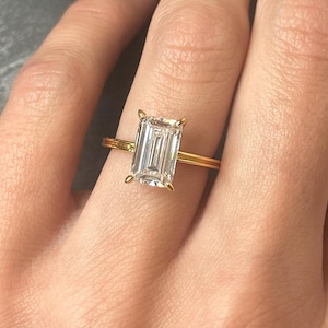 May include: A gold engagement ring with a large, clear emerald-cut diamond.