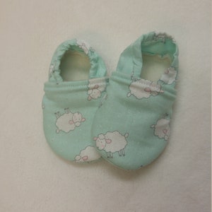 Peut inclure: Une paire de chaussons pour bébé de couleur bleu clair avec un motif de moutons blancs. Les chaussons sont faits d'un tissu doux et ont une coupe confortable.