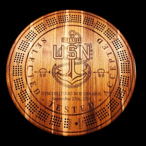 May include: A round wooden cribbage board with a dark brown finish. The board features the USN anchor emblem and the text "SELECTED ACCEPTED TESTED" around the edge. The center has the text "STSC(SS)TODD BONEBRAKE September 27th, 2024".