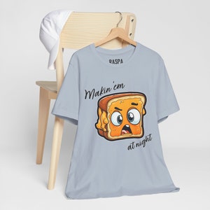 May include: A light blue t-shirt with a cartoon image of a grilled cheese sandwich with a face. The text "Makin' em at night" is printed below the image. The brand name "RASPA" is printed on the shirt.
